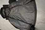 A black waterproof jacket with black trim and a hood, laid flat on a light gray marble surface.