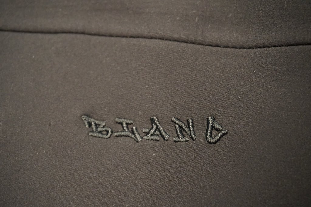 Close-up of a black fabric surface with the word 'BLANC' embroidered in matching black thread.