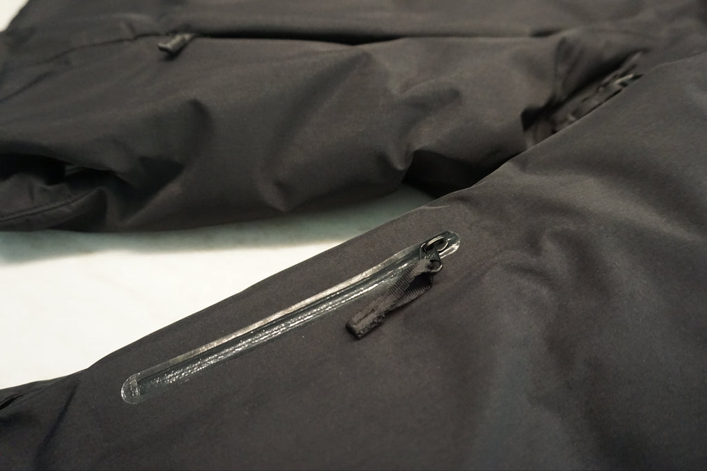Close-up of a black waterproof jacket showing a zippered pocket on the sleeve with a YKK waterproof zipper.