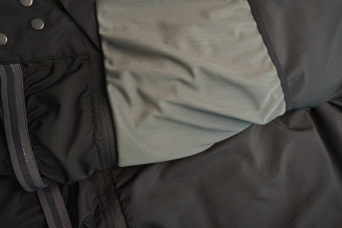 Close-up detail of a black puffer jacket showing a light gray elastic drop pocket.