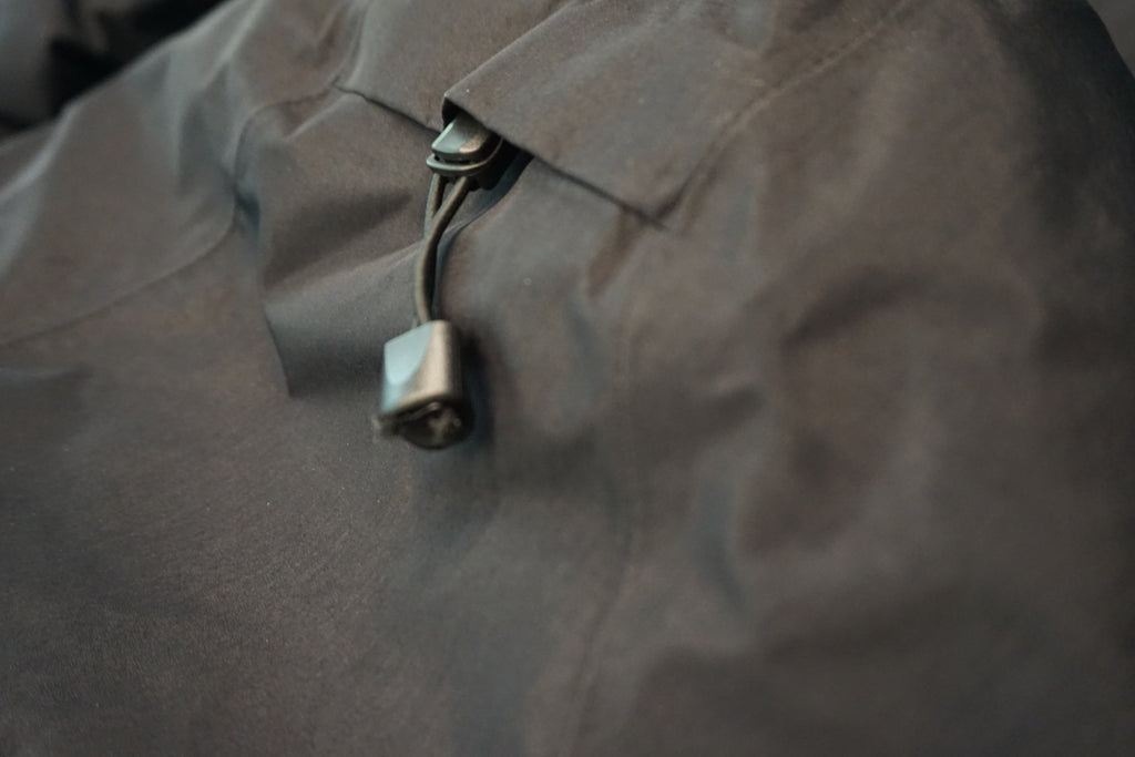 Close-up of a dark gray waterproof jacket with a black plastic toggle and cord on the hood to adjust the hood shape.