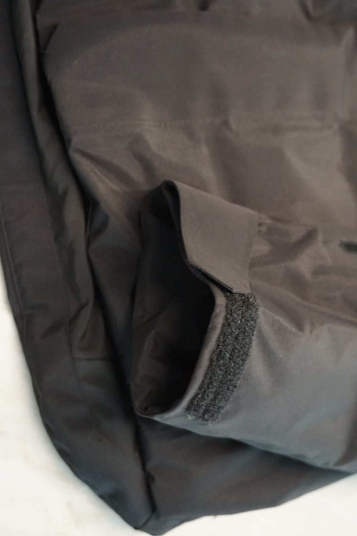 Close-up of a black waterproof jacket showing a reinforced seam and a hook-and-loop cuff closure.