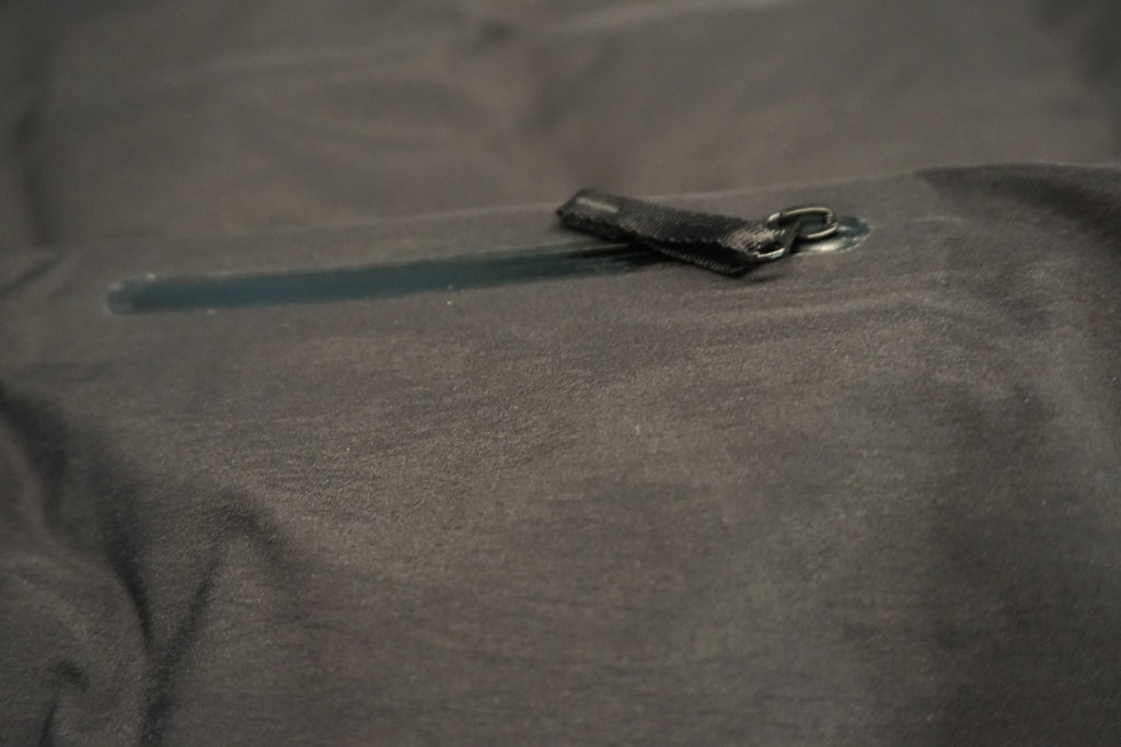 Close-up of a black waterproof jacket fabric with a horizontal zipper and a black zipper pull tab.