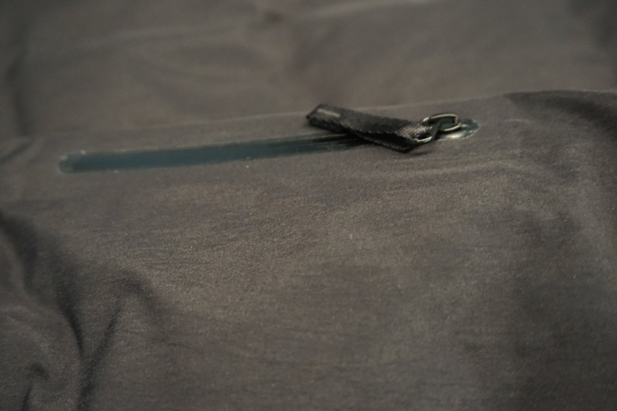 Close-up of a black waterproof jacket fabric with a horizontal zipper and a black zipper pull tab.
