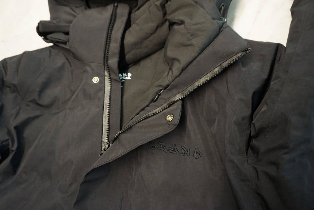 A close-up of a dark gray hooded jacket with a visible 'BLANC' logo on the chest, laid flat against a light background.